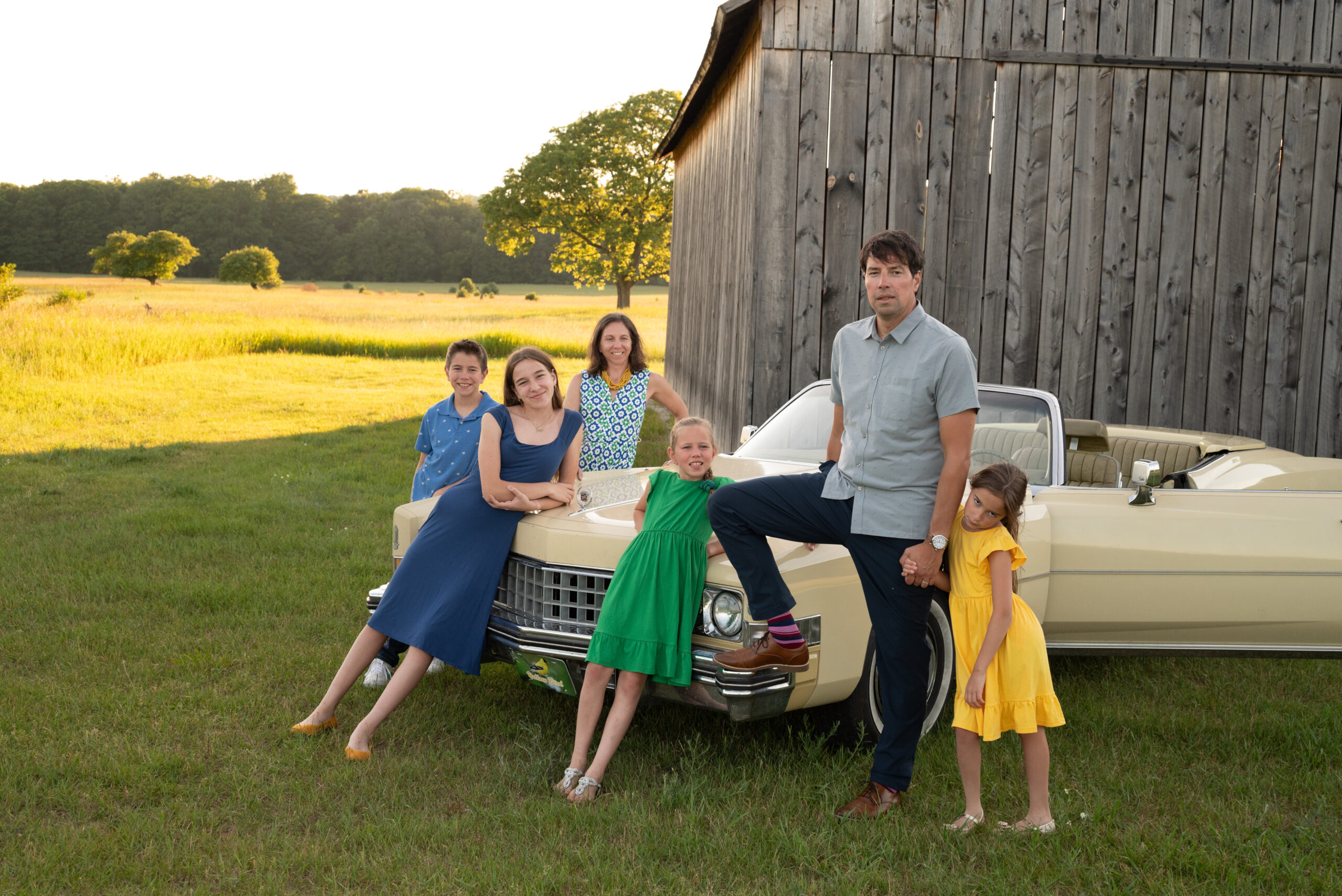 family of six photo with a 1970s cadillac and old barn