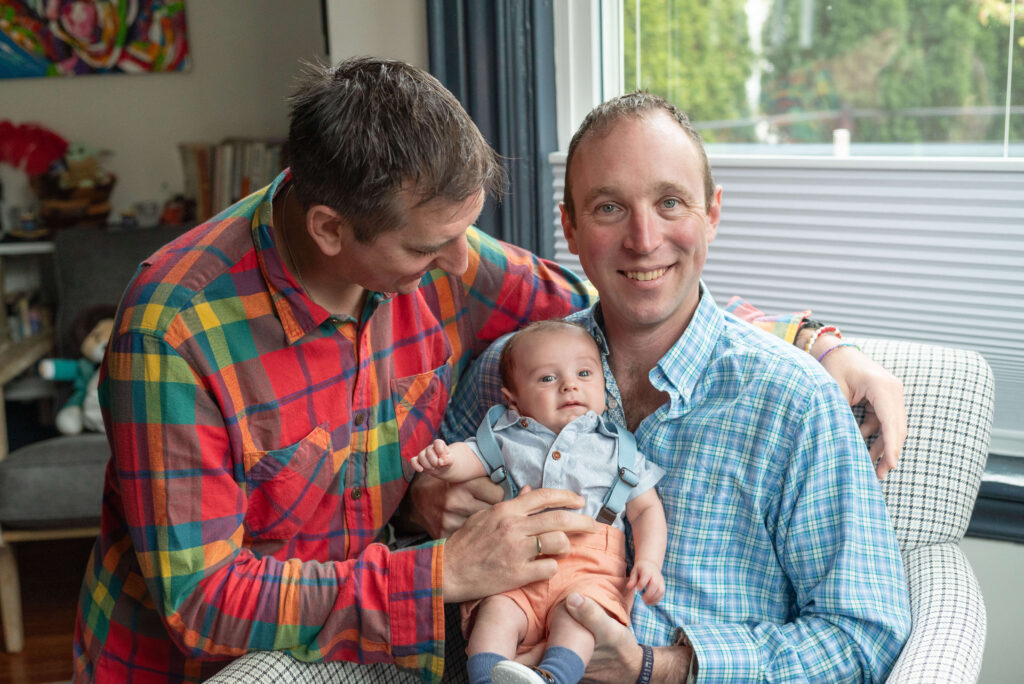 two dads holding infant son indoor family photo