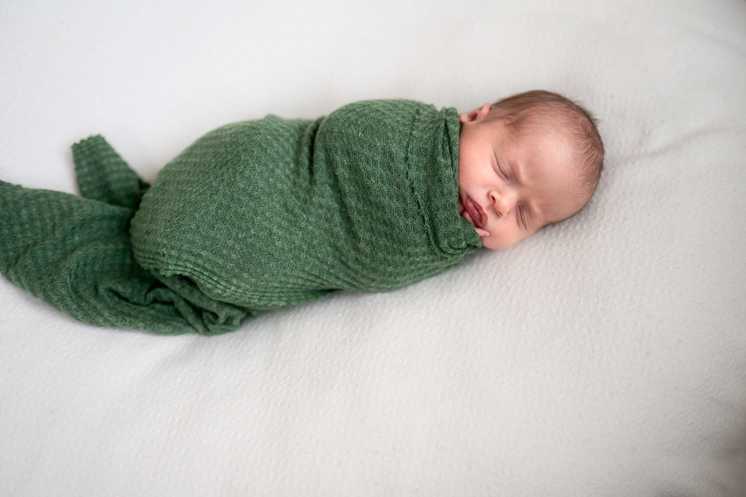 newborn swaddled in green blanket on large soft pillow