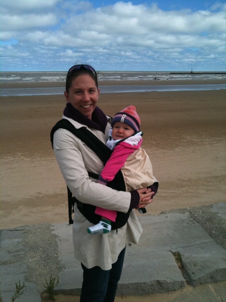 Essential baby stuff includes baby wearing items.  Here is a mother carrying infant using the ergobaby carrier along the shores of Lake Michigan.