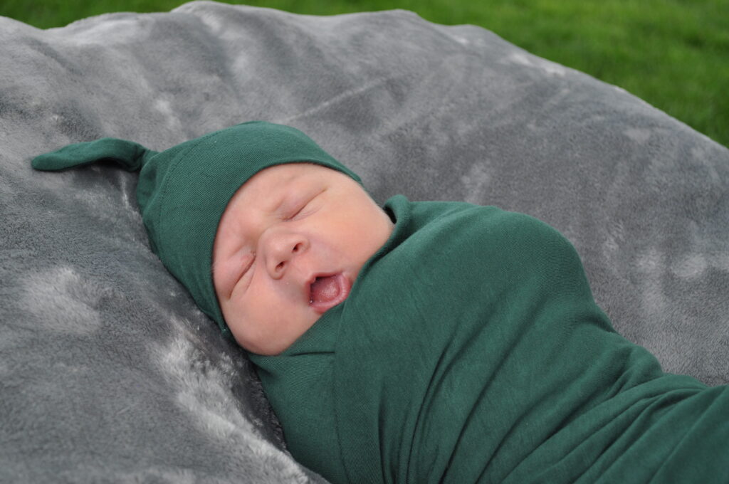 Essential gear includes swaddles. Infant swaddled in dark green wrap, matching hat, sleeping peacefully.