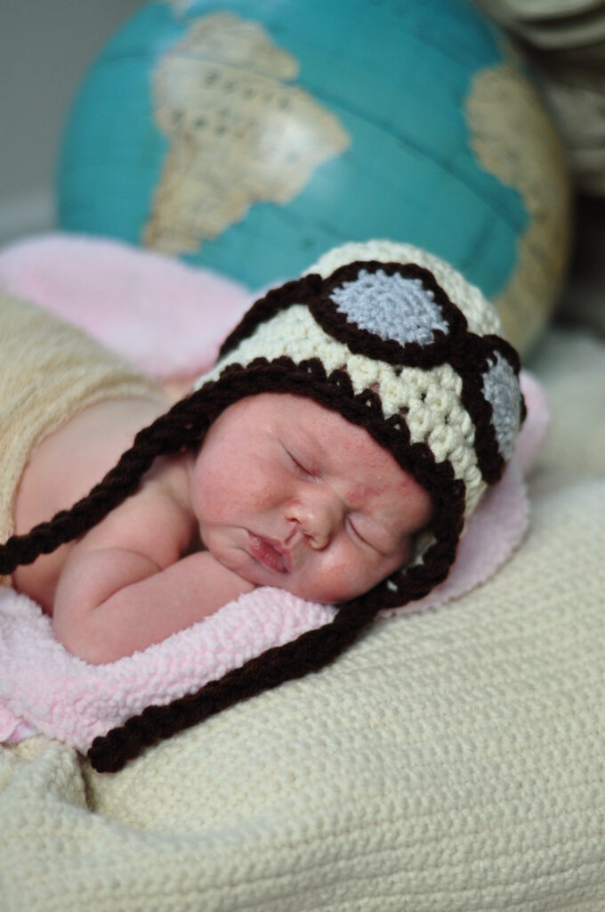 Infant wearing knitted pilot's hat, sleeping with globe in background.