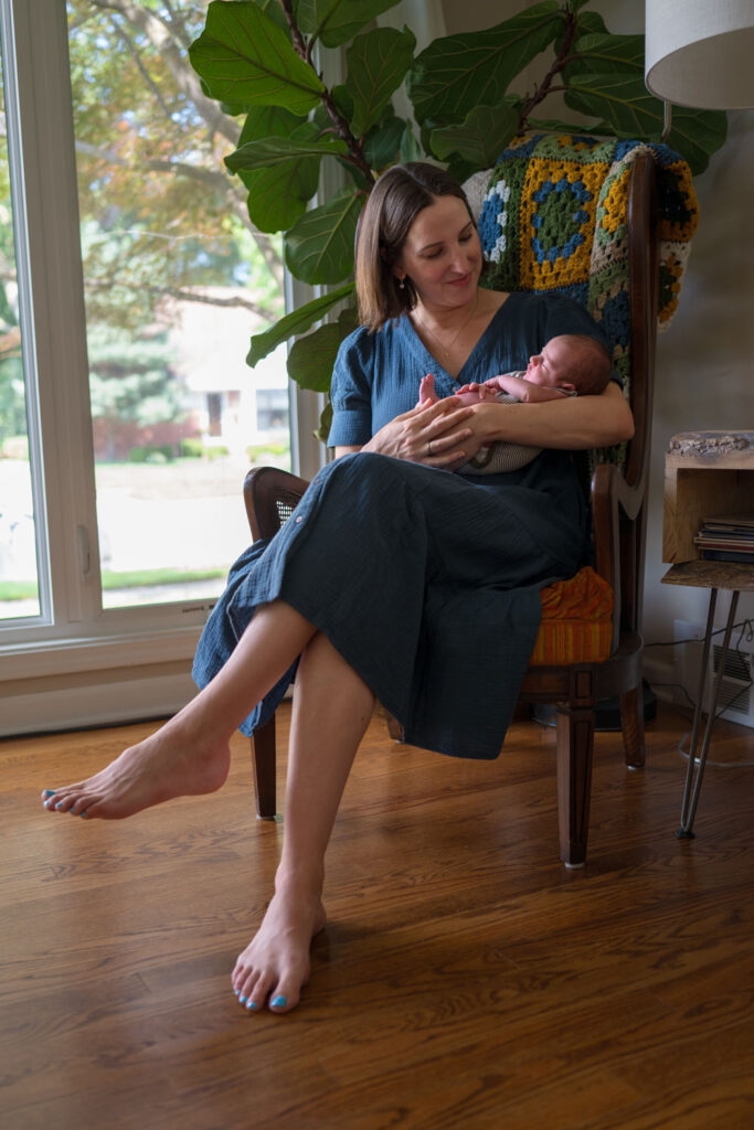A mother cradling her newborn baby in gentle window light during a quiet moment at home.