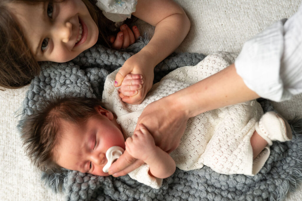 Big sister and mother doting on their newborn brother during a newborn photo session