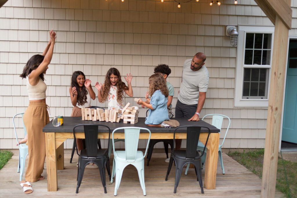 A joyful candid moment of a mother laughing with her children outdoors, playing jenga.