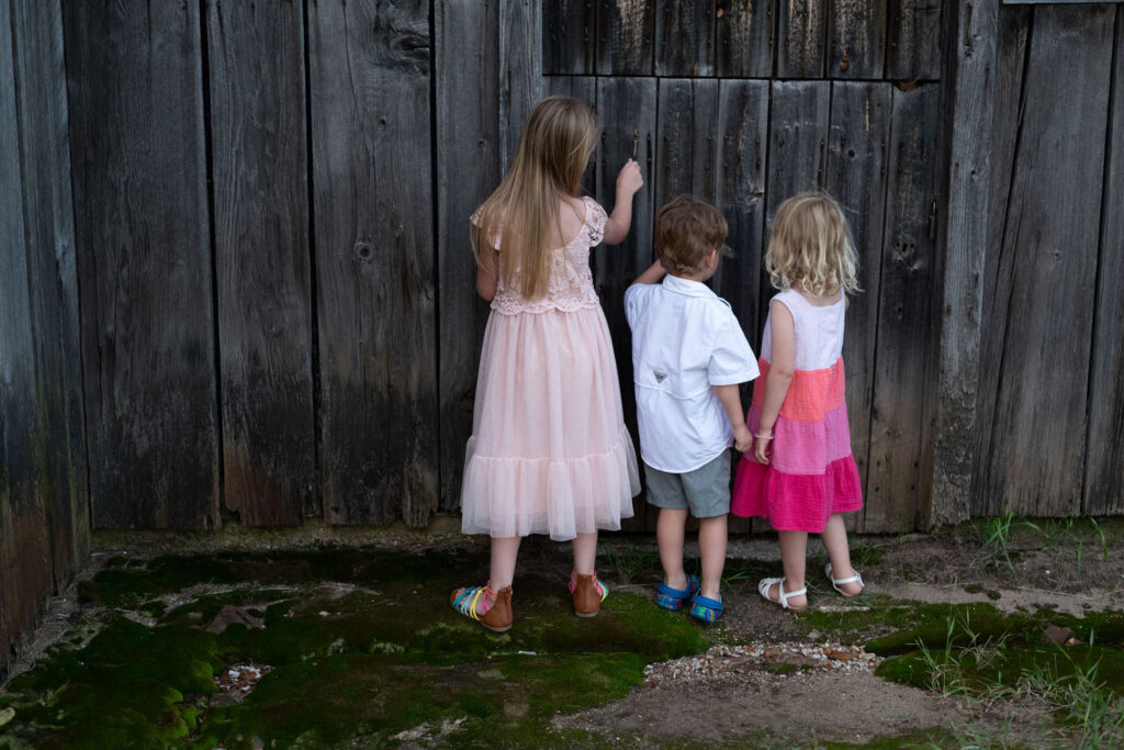 Three children in coordinated outfits outside a old barn.