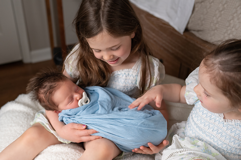 Sisters cuddling their newborn brother-images like this make perfect photo gifts for grandparents.