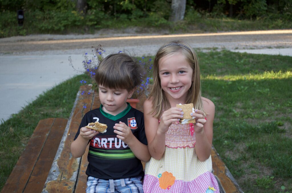 Two children eating s'more on a picnic table.