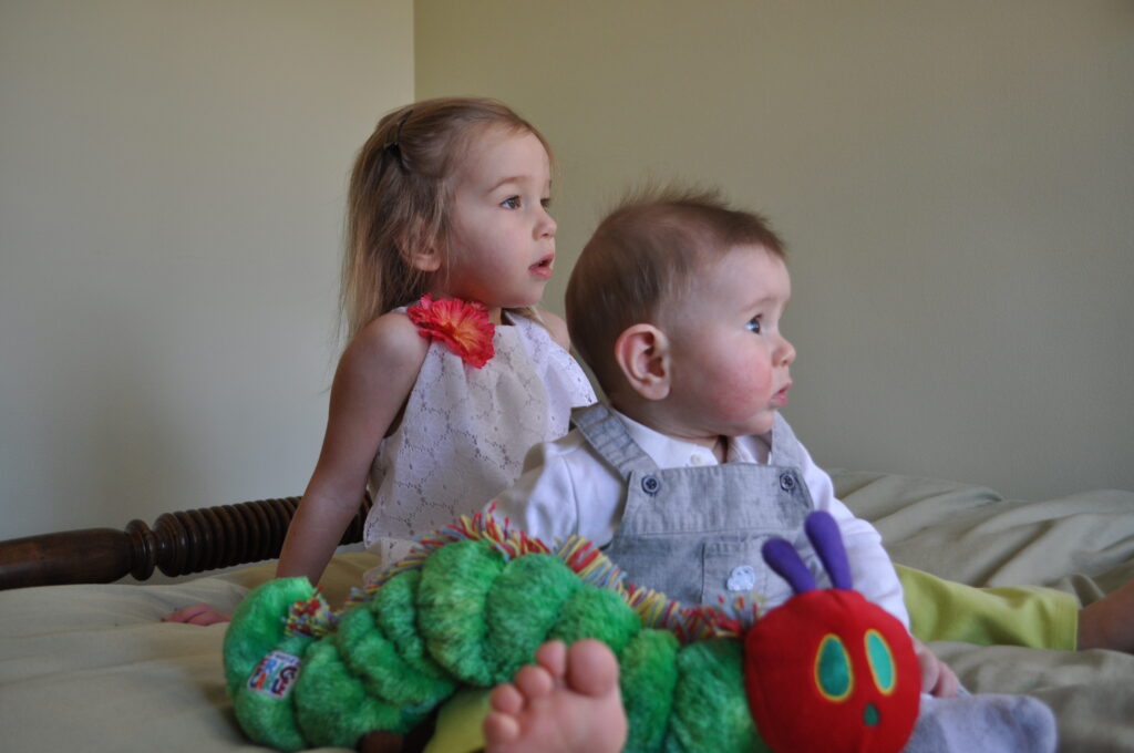 infant and todder sitting on bed with stuffed caterpillar toy