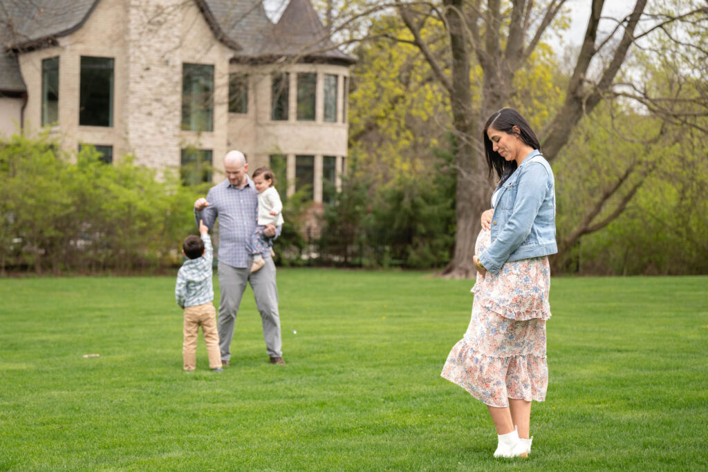 A glowing expectant mother standing in a field for her spring maternity photos, wearing a layers with pastel colored dress.