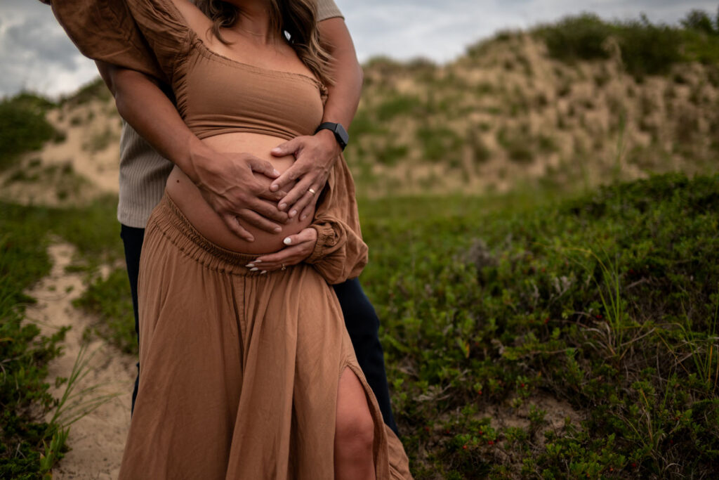 Close up of parents-to-be during a maternity photo session with their hands on the mother's pregnant belly with bluffs in the background.