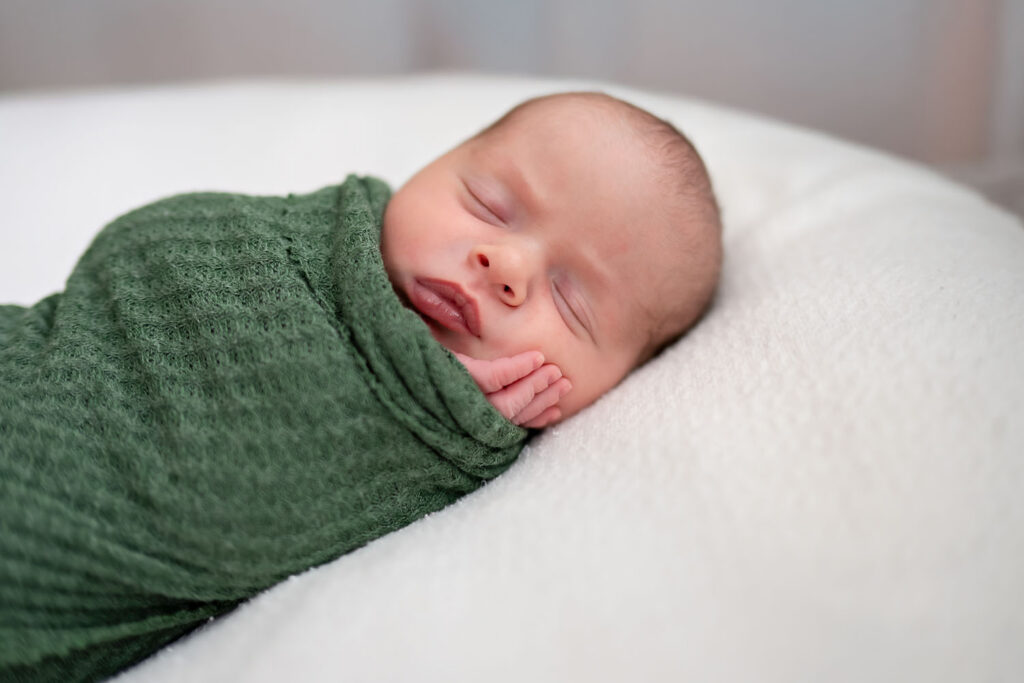 newborn sleeping in green swaddle during in-home photography session