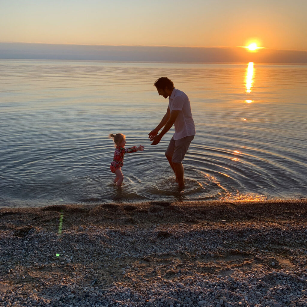 Father and daughter dancing in the gentle waves on Empire Beach during a sunset family photography session.