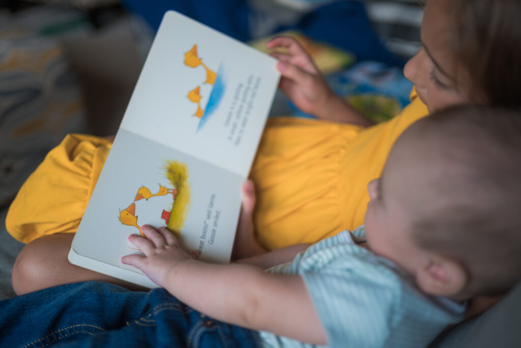 Older child reading to an infant during an in-home family session shows a childhood milestone of learning to care for others