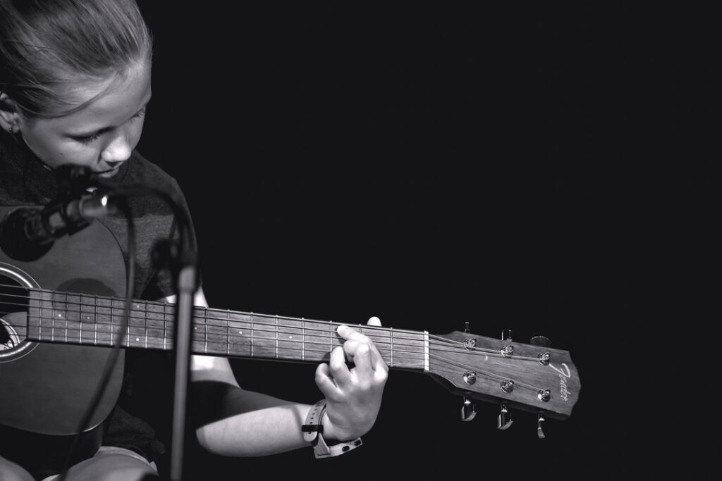 Girl on stage playing a guitar on her own celebrating brave new childhood milestones.
