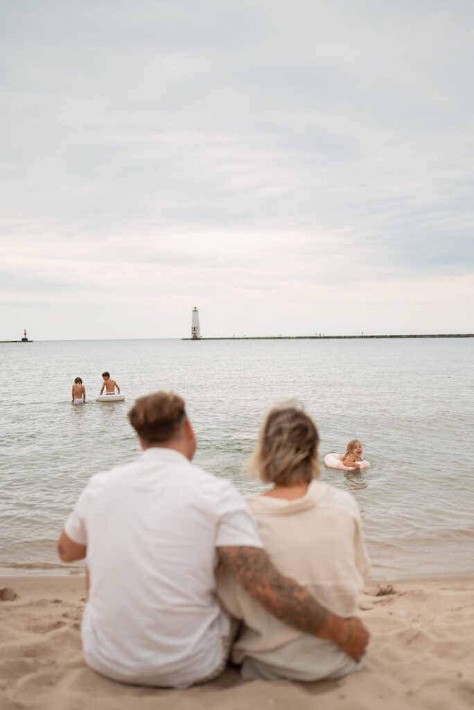 Parents watching their children play together without them during a family beach photo session.